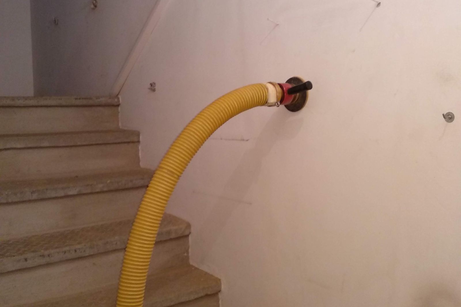 Tubo giallo di insufflaggio innestato in un foro sulla parete di un vano scala con gradini in marmo
