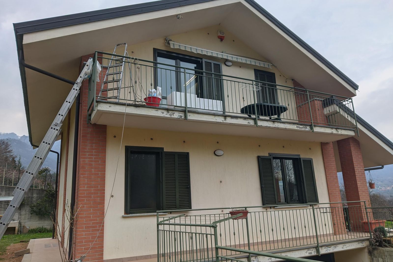 Facciata di una casa bifamiliare con intonaco chiaro e fasce rosse, a lavoro concluso