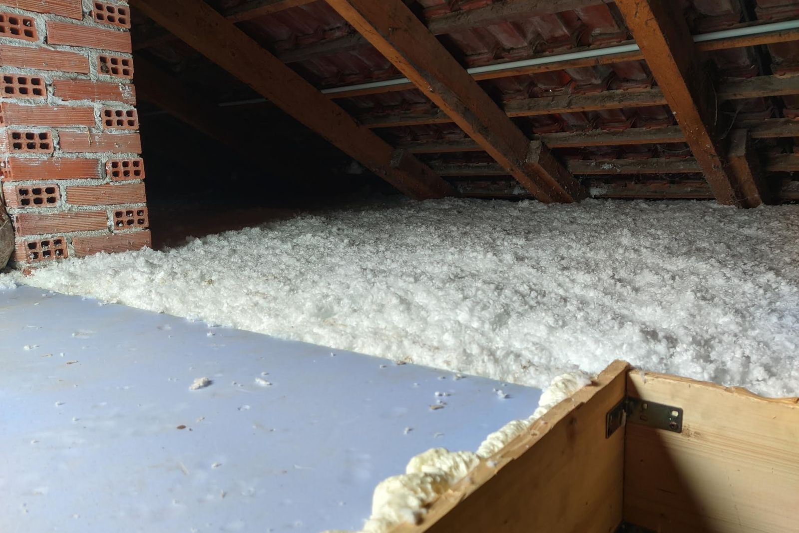 Sottotetto con travi in legno e coltre di isolante bianco stesa sul solaio